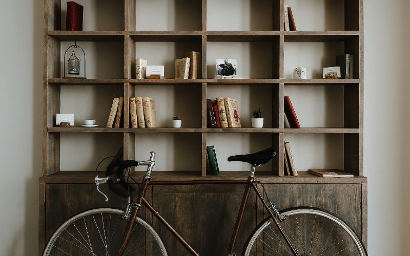 Libreria in legno con libri e oggetti decorativi, davanti a cui è parcheggiata una bicicletta da corsa vintage.
